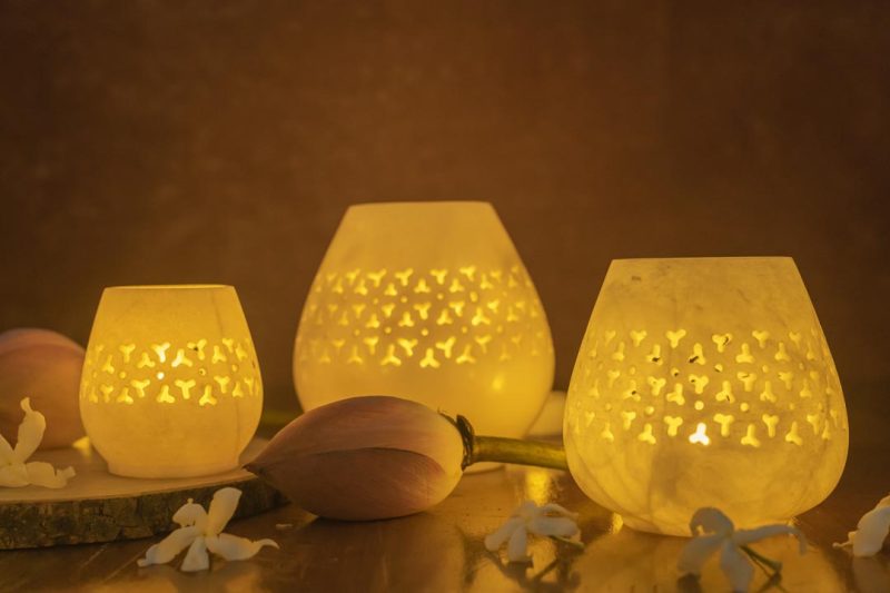 Jaali Blaze large candle holders in varying sizes, emitting a warm, patterned glow, set against a dusky backdrop with delicate floral embellishments