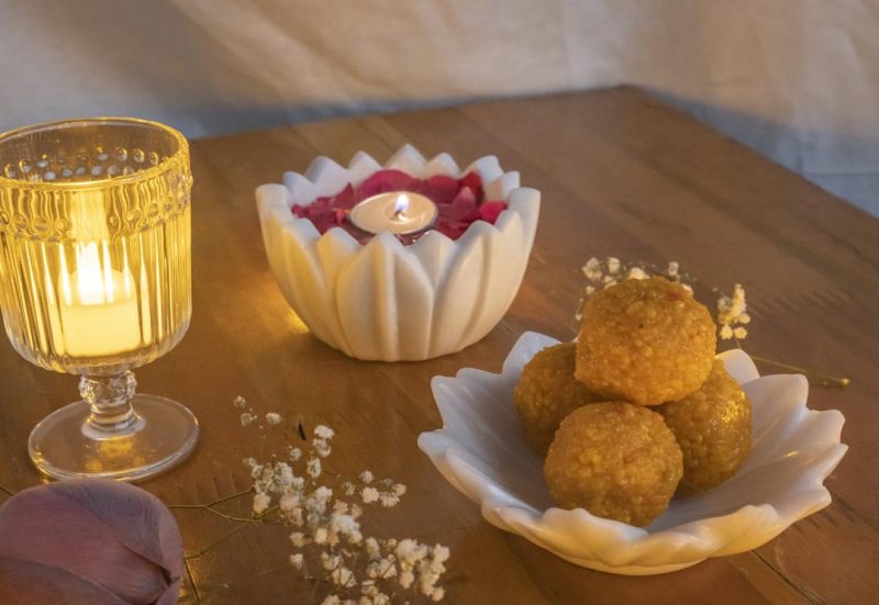 Cozy ambiance with Natural Handicrafts' Hover Petal Candle Floater, lit candle amidst rose petals, paired with golden laddus, enhancing the warm glow of a tranquil evening.