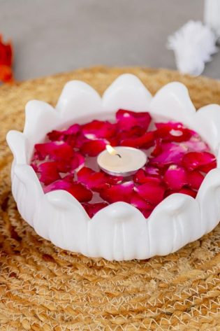 Elegant Ooze Candle Floater in white with vibrant red rose petals and a lit candle, set on a natural jute table mat, perfect for creating a peaceful ambiance.