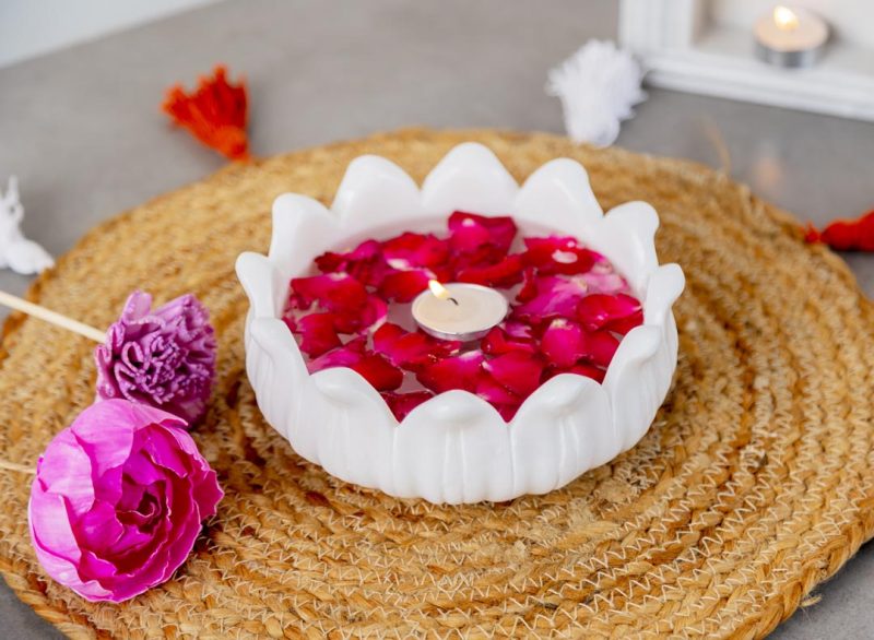 Elegant Ooze Candle Floater in white with vibrant red rose petals and a lit candle, set on a natural jute table mat, perfect for creating a peaceful ambiance.