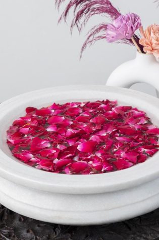 Traditional white Urli Candle Floater brimming with vivid pink rose petals, accompanied by modern white sculptures, merging classic and contemporary decor styles.