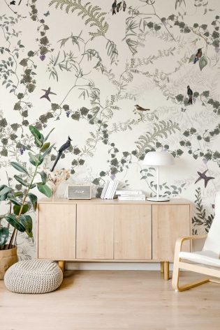 Wallpaper named 'Vineyard' displaying a charming scene of greenery and birds, offering a peaceful and natural touch to a bright and modern room design.