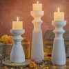 Tall white marble standing candle holders set by Natural Handicrafts, with lit candles, complemented by rustic baskets and a warm backdrop, for an elegant home decor.