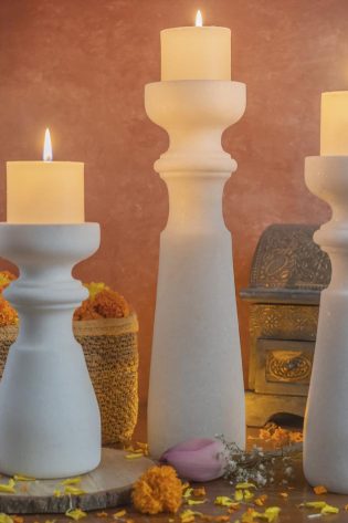 Tall white marble standing candle holders set by Natural Handicrafts, with lit candles, complemented by rustic baskets and a warm backdrop, for an elegant home decor.