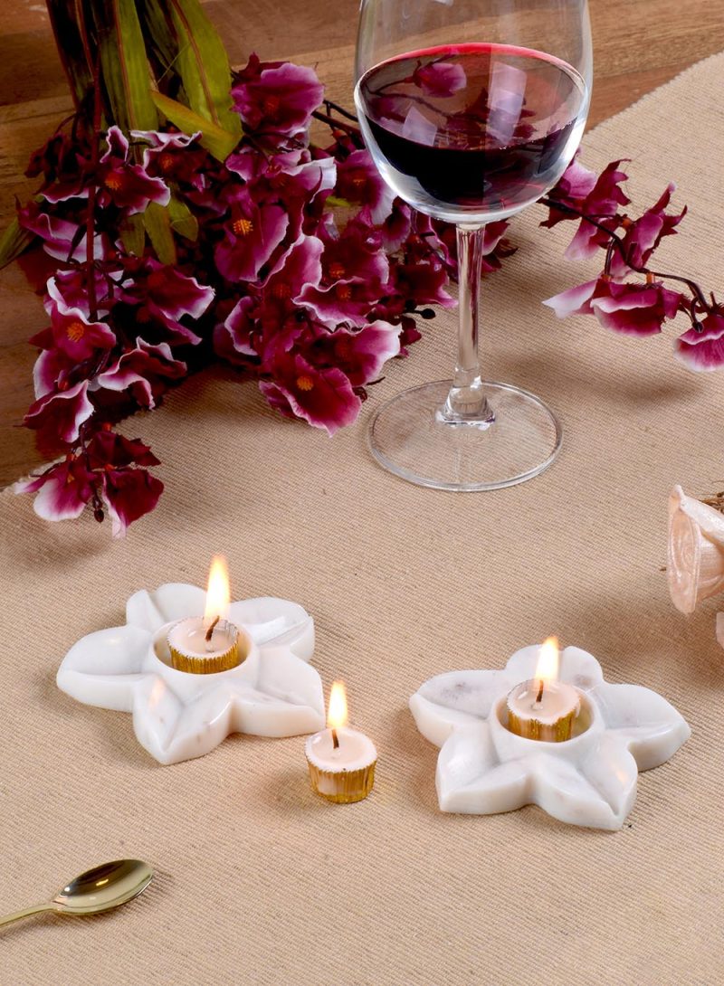 Delicate white marble 'Starlight' candle holders by Natural Handicrafts, with small tea candles lit, enhancing the floral ambiance on a textured tablecloth.